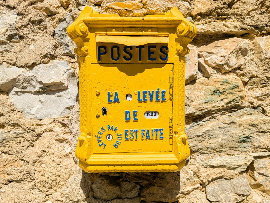 Classic yellow French mailbox on stone wall in sunlight, perfect for travel or historical themes.